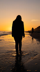 kobieta idąca brzegiem morza na tle wschodzącego słońca 