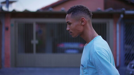 One introspective young black walking forward in street in thoughtful contemplation. Tracking shot in motion of a pensive South American Brazilian person thinking about life
