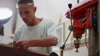 One Brazilian black young carpenter working at woodworking carpentry workshop next to industrial machine, job occupation of apprentice engaged at work