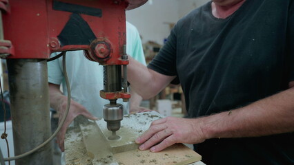 Senior Carpenter using industrial machine to make a hole into wooden surface, woodworking job...