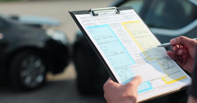 Close up of a man car insurance agent inspecting damaged car withagreed statement of facts on motor vehical accident form. Male filling in a car repair claim. Insurance concept.