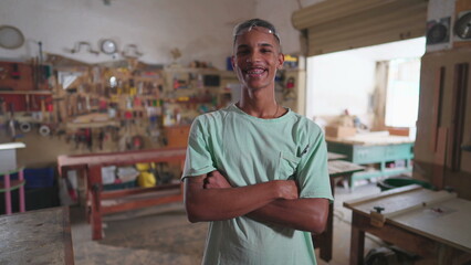Joyful Brazilian Carpenter Smiling at Camera in Workshop, Arms Crossed, tools in background. job occupation portrait