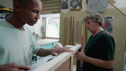 Obraz premium Carpenters working at workshop. Senior and young employee polishing wooden furniture, authentic Brazilian small business in South America