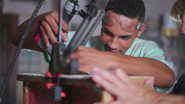Master carpenter guiding young apprentice to build craftmanship furniture at carpentry workshop. Diverse collaboration between an older man and junior pupil