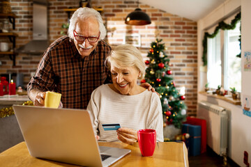 Senior caucasian couple online shopping on their laptop with a credit card during christmas and the...
