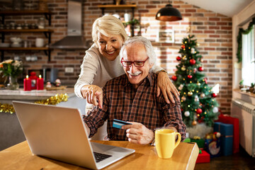 Senior caucasian couple online shopping on their laptop with a credit card during christmas and the new year holidays