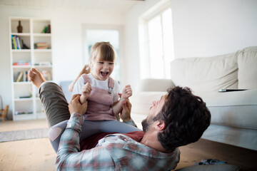 Young caucasian father and daughter hugging and playing together in the living room at home