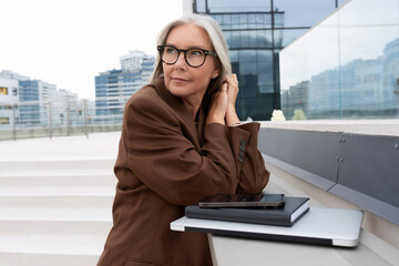 confident mature old lady with gray hair in glasses wearing a brown jacket is waiting for a...