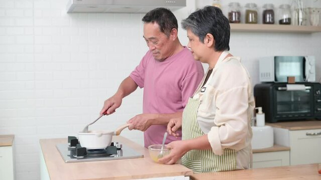 Happy Asian senior couple cooking together in kitchen, Making eggs for breakfast