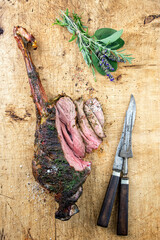 Traditional barbecue dry aged haunch of venison with herbs served as top view on a wooden board - obrazy, fototapety, plakaty