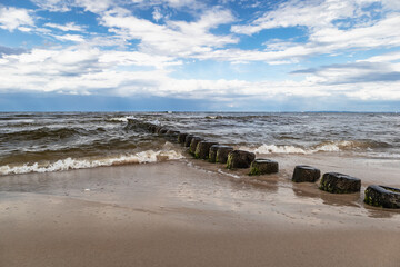 Brzeg Morza Bałtyckiego z falochronami i błękitnym niebem z chmurami.
Baltic sea shore with breakwaters and blue sky with clouds.