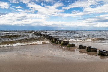 Brzeg Morza Bałtyckiego z falochronami i błękitnym niebem z chmurami. Baltic sea shore with breakwaters and blue sky with clouds.
