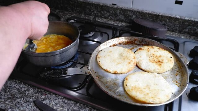 Woman's hand prepares three arepas and an egg for breakfast on the kitchen stove