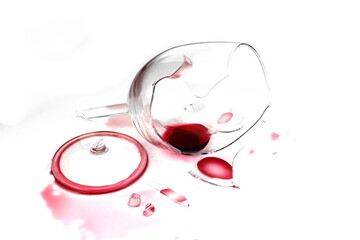 Broken glass and spilled red wine on white background