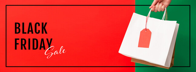 Black Friday sale banner. Female hand holding two shopping bags with price tag on red and green background