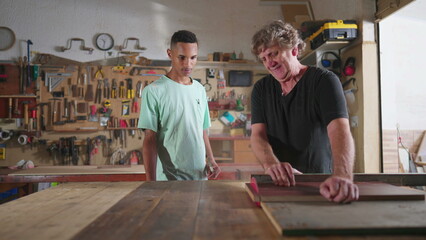 Carpenter and apprentice working at workshop, teacher orienting young man with saw machine at carpentry. Wood sawing scene of mentor teaching student