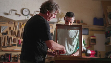 Fototapeta premium Senior carpenter at work with young apprentice, candid scene of carpentry workshop, job occupation craftmanship concept