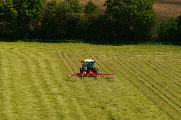Obraz premium Tractor turns over freshly cut hay for drying.