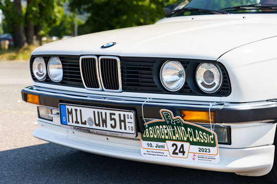A vintage BMW E30 325i convertible stands in the parking lot. Front view of the grille, hood, headlights and bumper.