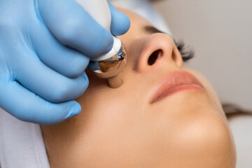 Close up expert applies hardware face massage for rejuvenation to beautiful woman. 