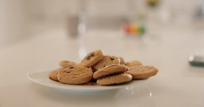 Hands, cookies and plate on table in home kitchen, eating or hungry for sweets at breakfast. Closeup, biscuits and sugar food of person, dessert or confectionery snack for unhealthy diet in nutrition