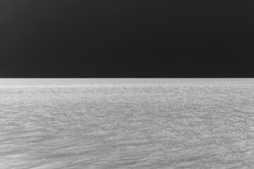Looking out over the water in a minimalist view with a sky and horizon line in black and white film...