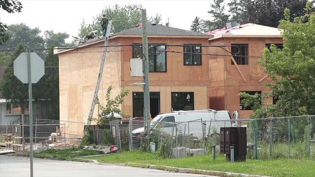 roofers workers doing roof applying shingles on new home being built without wall finishing, ladder van fence trees grass