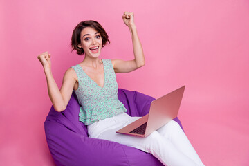 Portrait of successful young gamer woman raise fists scream yell victory hooray yeah lying comfort...