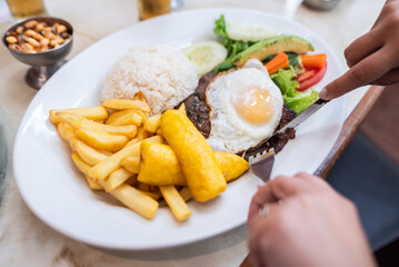 hands cutting the meat of a steak to the poor. Traditional Peruvian food