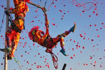 A man in a beautiful punk acrobat costume in the air on a rope in flight performs tricks and poses for the carnival. Against the background of fireworks candy and the sky. 