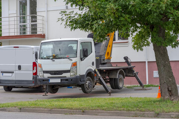 "Lewitujący" na podporach hydraulicznych samochód ekipy montującej klimatyzację , latem przed budynkiem w okół dużo zielonych drzew i innej roślinności miejskiej. © Grzegorz