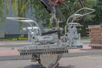 Przyżąd do mechanicznego układania kostki brukowej - hydrauliczna układarka - i krawęzników zamontowany na koparce . W strugach letniego deszczu . © Grzegorz
