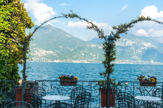 Sun on mountain side across Lake Como through vines over arches on lake edge Menaggio, Italy.