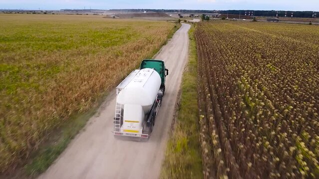Aerial 4k drone tracking shot of Bulk Dry Cement trailer truck driving down a dusty rural road. Construction machinery off road. Cement powder transported to remote construction site among farms.