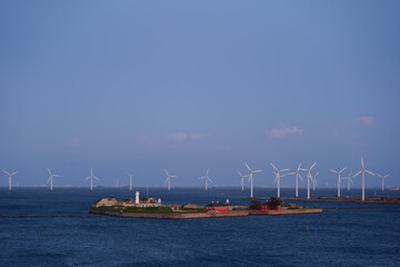 Outdoor aerial exterior panoramic seascape view of Trekroner Fort and row of offshore wind power station farm during twilight time.
