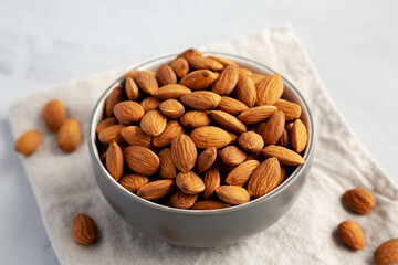 Raw Organic Almonds in a Bowl on a gray background, side view.