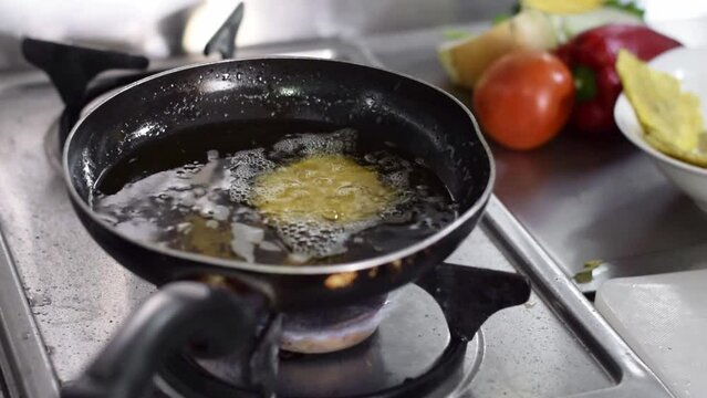 close-up of a woman's hand, throwing flattened pieces of plantain into the frying pan to fry and prepare patacones.