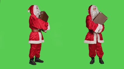 Santa claus in costume with suitcase, waiting for transportation over full body greenscreen backdrop. Young man acting like father christmas and carrying vintage briefcase, holiday concept.