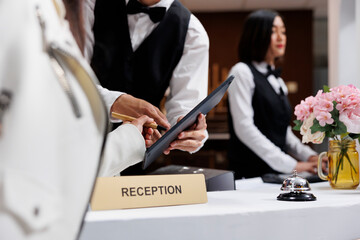 Asian male receptionist at contemporary hotel helps customer sign registration form. Booking hotel...