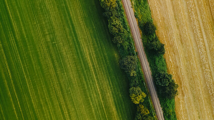 Aerial top down view of railway road among agricultural fields in summer day. 