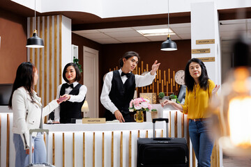 Tourists arriving at their holiday destination being assisted by friendly staff members. Guest offering passport for check while other tourist receives room directions by male receptionist