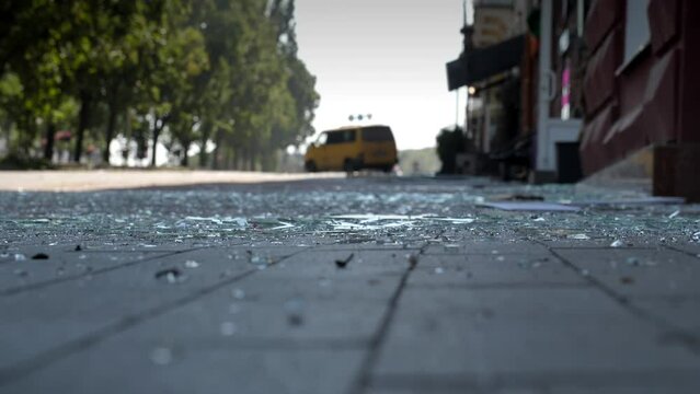 Close-up of glass shards on a pedestrian pavement made of paving stones against the background of a broken car. The result of an explosion, accident or catastrophe.