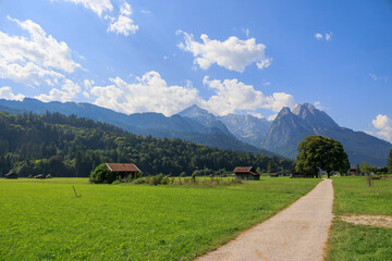 Field path near Garmisch-Partenkirchen with view to the Zugspitz massif on a sunny day with blue sky and white cumulus clouds