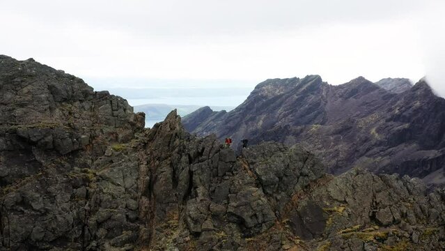 Aerial view of hikers climbing and traversing the jagged peaks of the alpine Cuillin ridge on the Isle of Skye Scotland. Scenic backdrop with mountains, lochs and sea. Moody day.