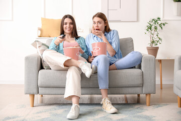 Female friends eating popcorn on sofa at home