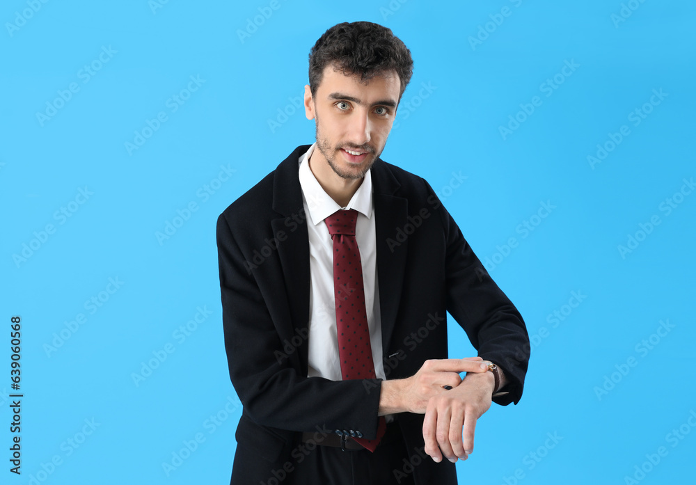 Wall mural Young man in suit looking at wristwatch on blue background