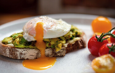 Poached egg over smashed avocado on sourdough toast with a side of grilled cherry tomatoes on the...