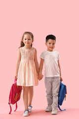 Cute little pupils with backpacks holding hands on pink background