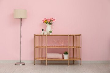 Chest of drawers with floor lamp, houseplants and stylish decor in shape of word HOME near pink wall