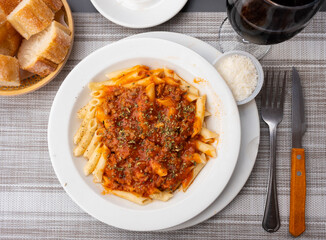 Penne pasta with tomato sauce, parmesan cheese and basil on white plate. Top view